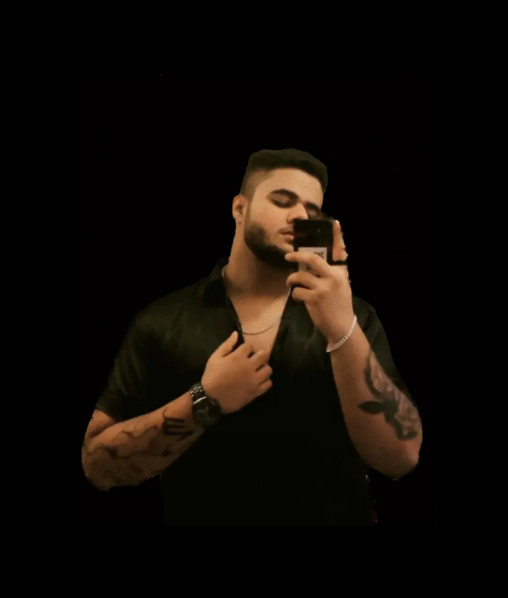 Amritash in a black shirt with tattooed forearms, against a black background