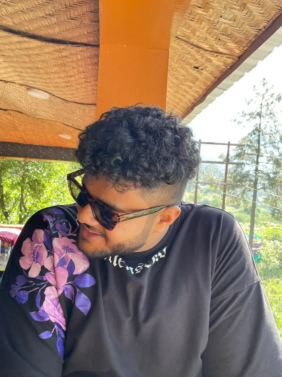 Amritash smiling, in tortoiseshell sunglasses and a black floral T-shirt
