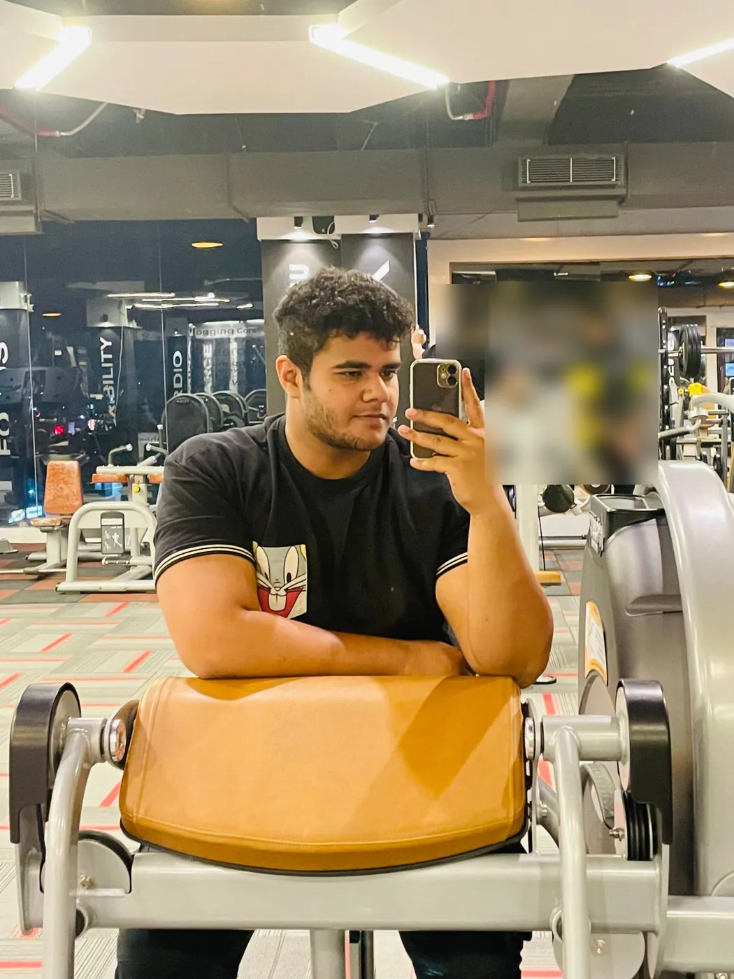 Mirror selfie of Amritash in a black T-shirt, leaning on a gym machine