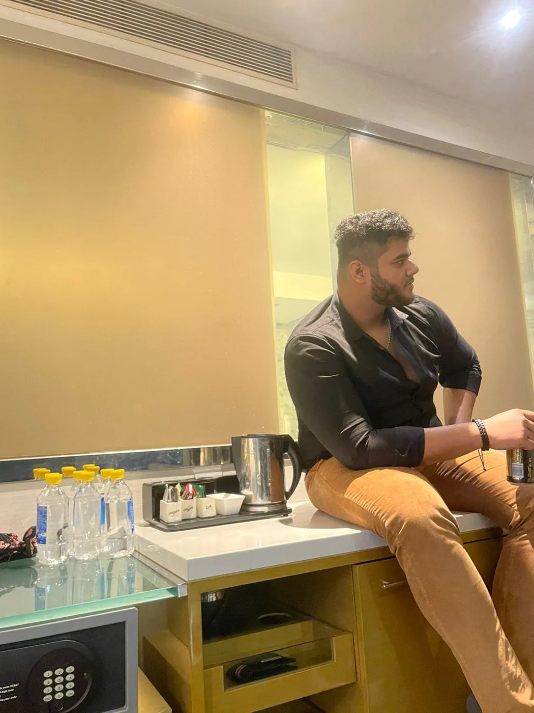 Amritash in a black shirt and tan trousers sitting on a hotel-room counter, looking to the side