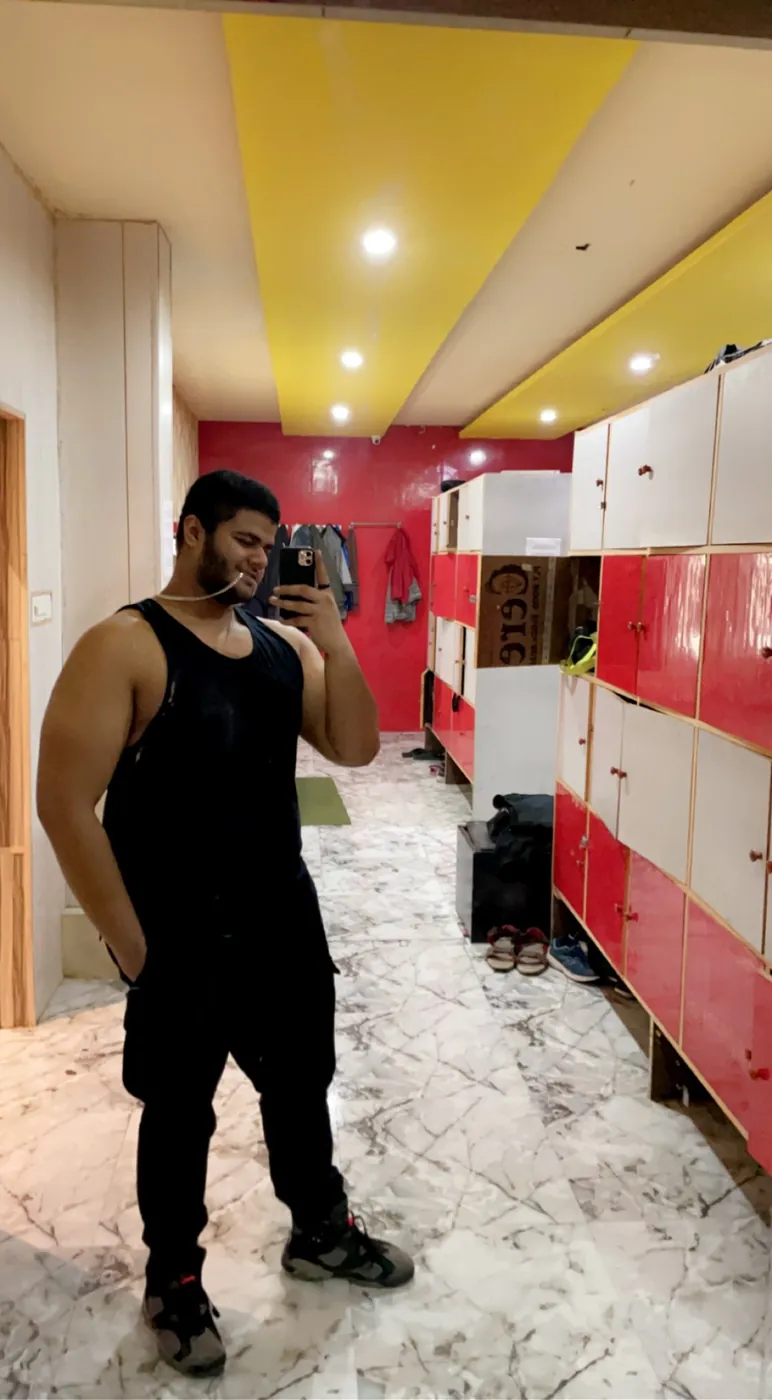 Mirror selfie of Amritash in a black tank top in a gym locker room