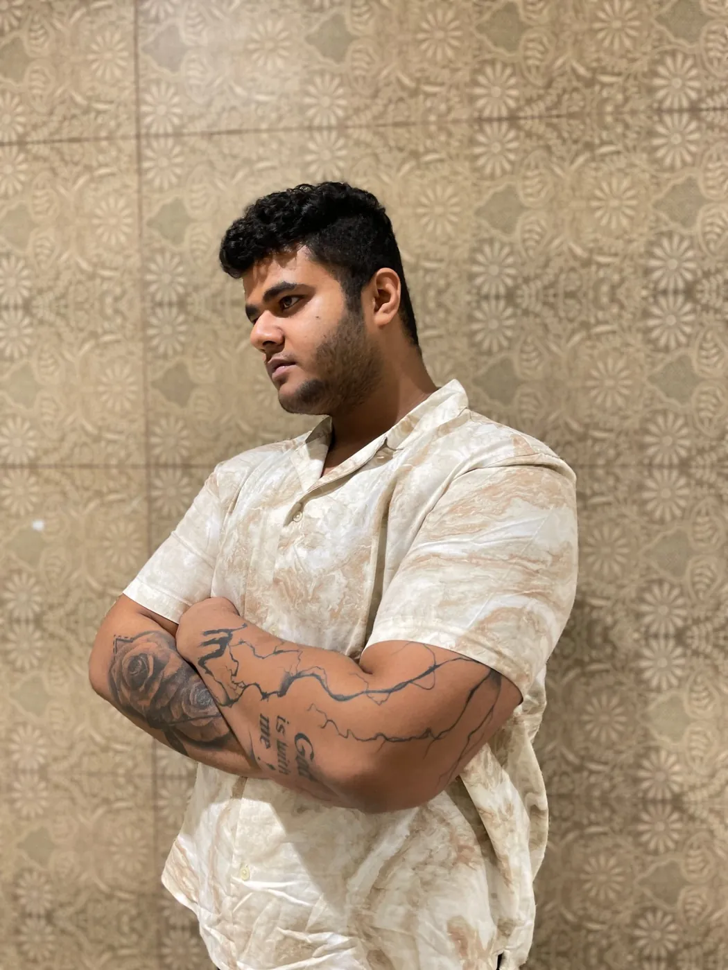 Amritash in a marble-print shirt with arms crossed, tattoos on both forearms