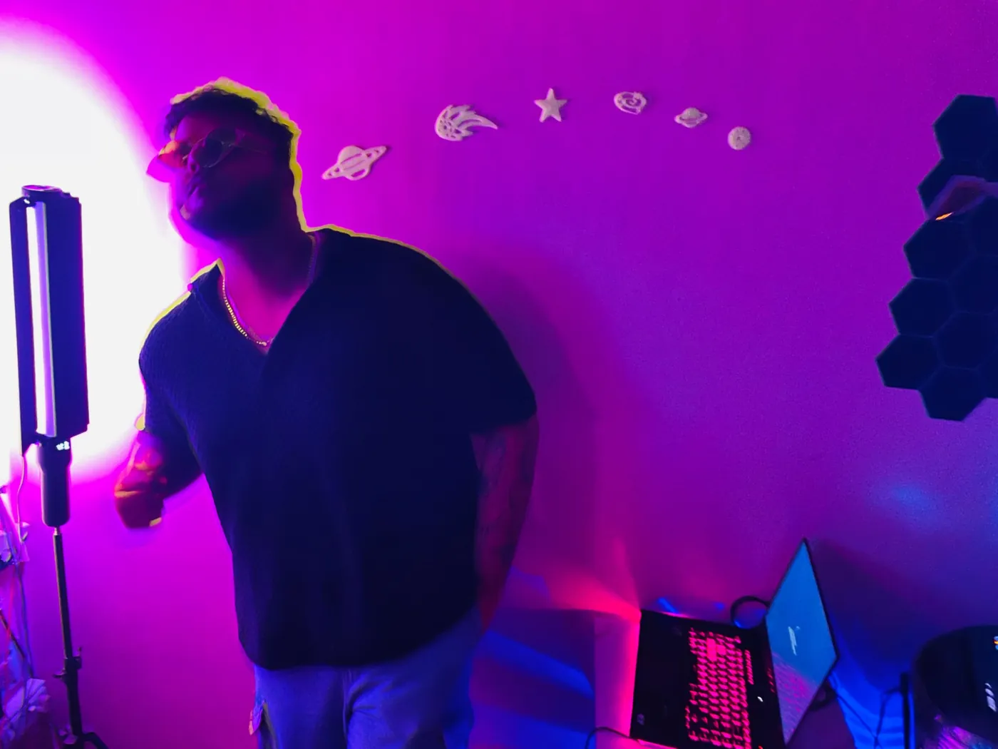 Amritash in a studio lit purple and pink, with a laptop and lighting rig