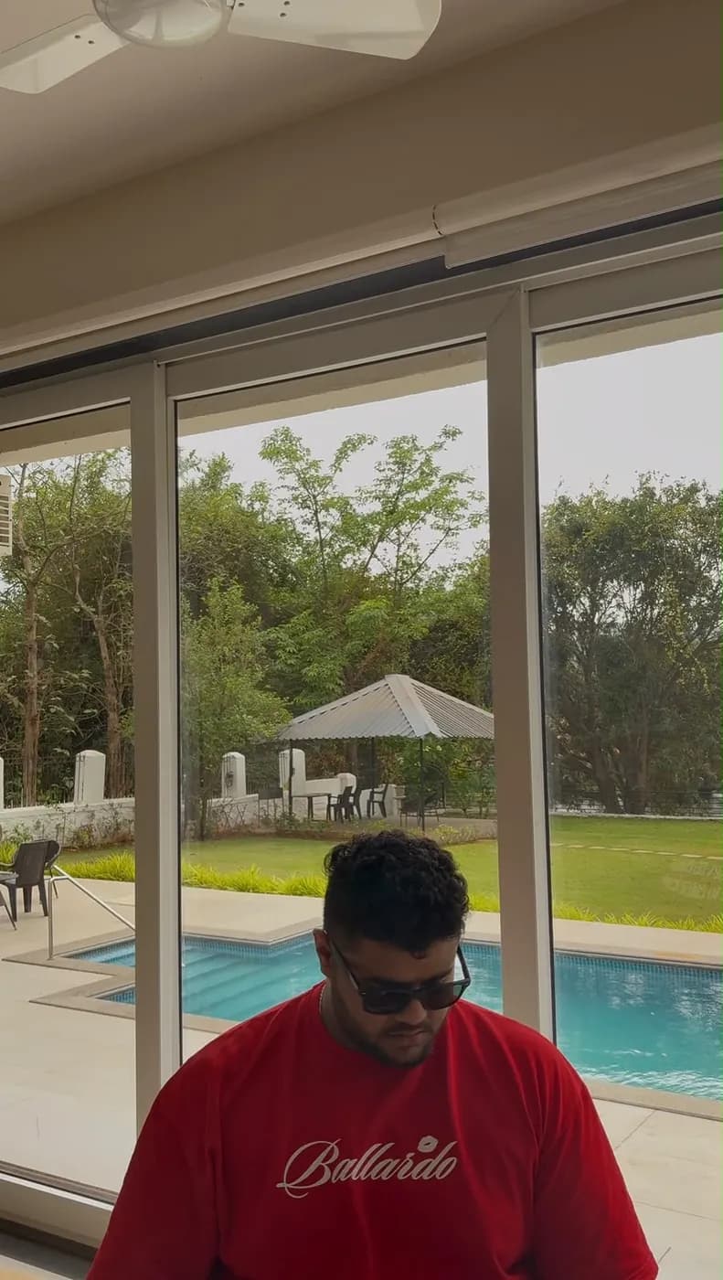 Amritash in a red T-shirt and sunglasses in front of glass doors, a pool outside
